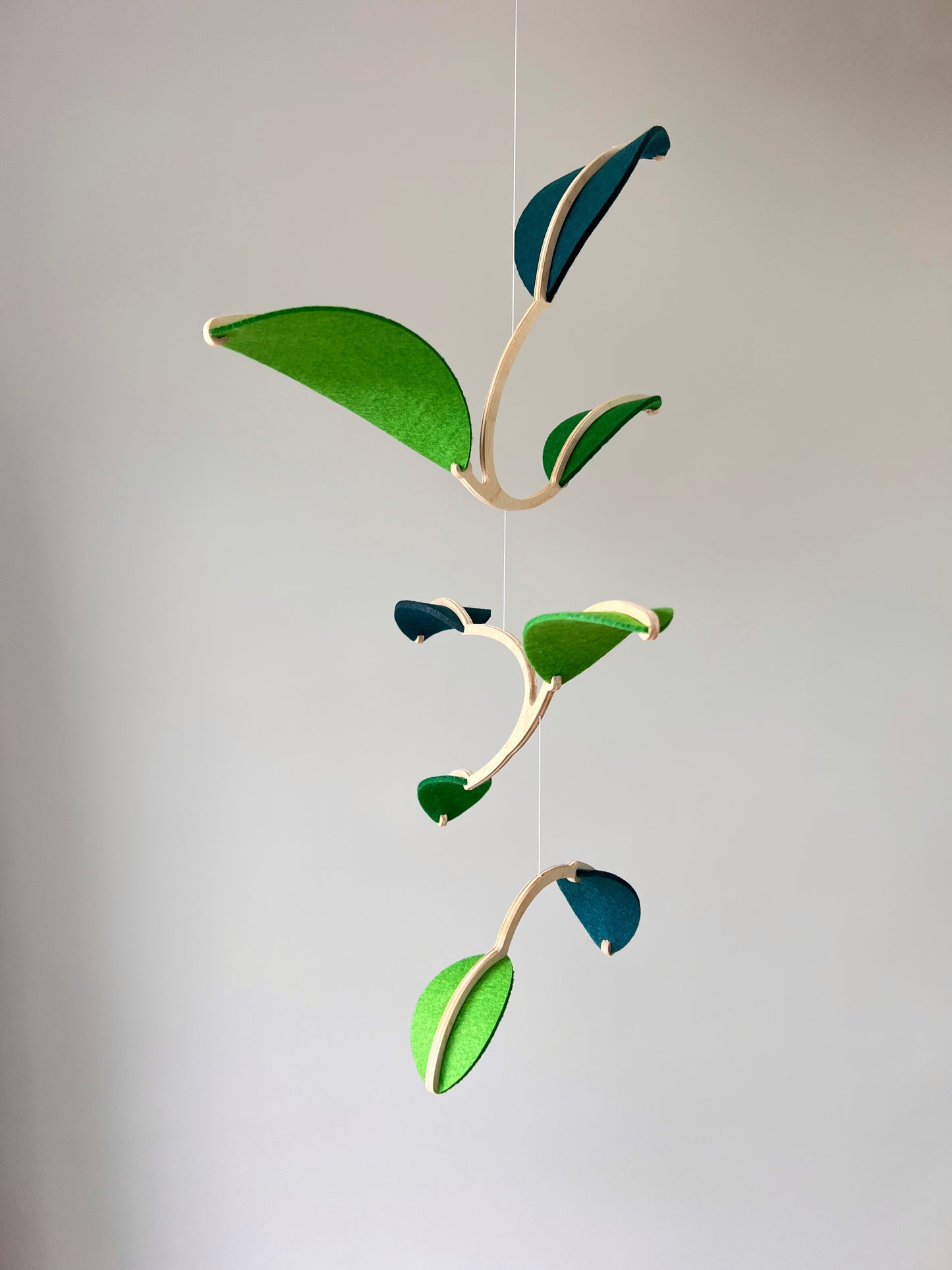 Felt Leaf Mobile
Elevate your space with this versatile Midcentury Modern Mobile, designed for both nurseries and adult living areas. Crafted from natural wood with deep teal and green shades of soft felt, this handmade nursery mobile embodies a minimalist and Scandinavian aesthetic. Its unique geometric design creates a stunning hanging sculpture that fits seamlessly into nursery decor and neutral relaxing spaces.