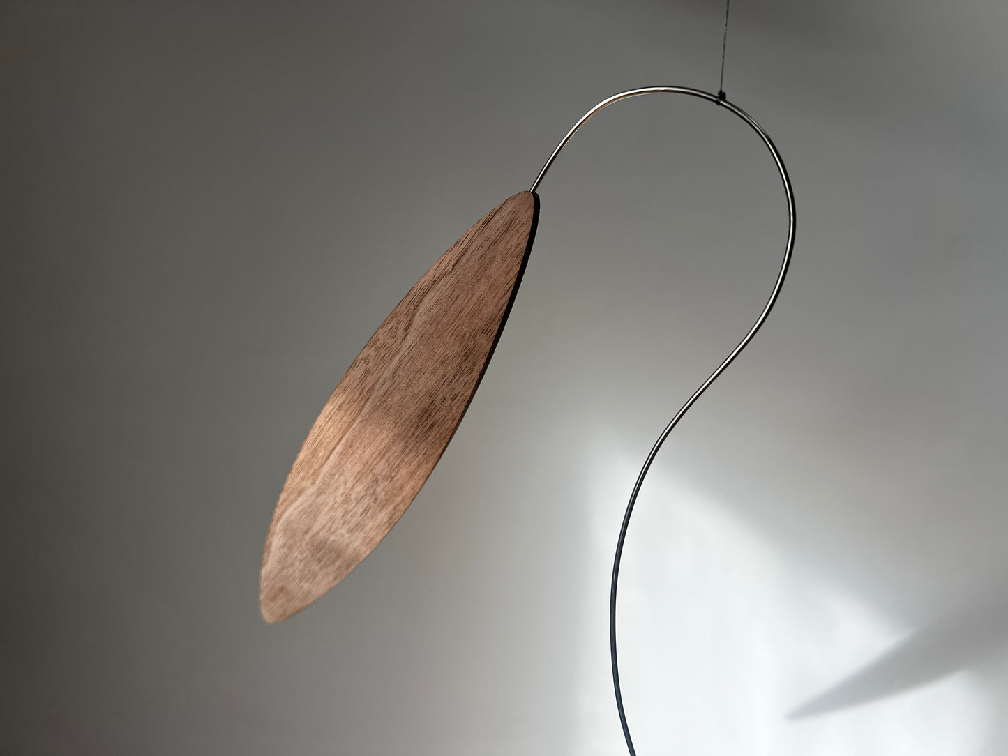 Large 1 metre walnut leaf mobile hanging on a wall beside artist, handcrafted layered walnut veneer wooden mobile with curved leaf forms and stainless steel wire, modern kinetic sculpture, moving art for adults, mid century decor, Scandinavian design minimalist decor, Calder inspired art mobile, unique designer home decor, wood hanging art for living room, gallery wall decor, contemporary mobile handmade in the UK by The Illuminist, soothing balancing art and modern wood art