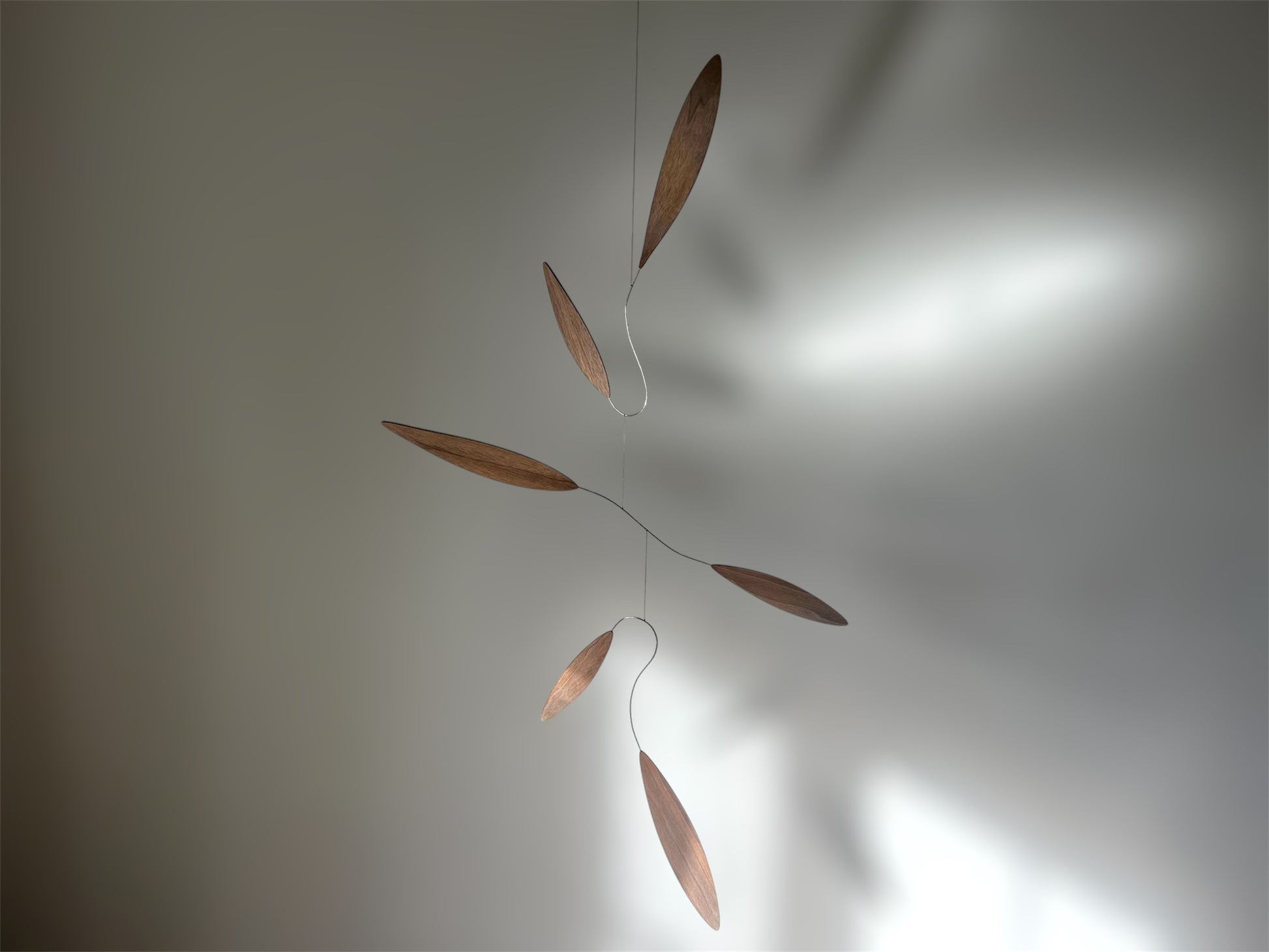 Large 1 metre walnut leaf mobile hanging on a wall beside artist, handcrafted layered walnut veneer wooden mobile with curved leaf forms and stainless steel wire, modern kinetic sculpture, moving art for adults, mid century decor, Scandinavian design minimalist decor, Calder inspired art mobile, unique designer home decor, wood hanging art for living room, gallery wall decor, contemporary mobile handmade in the UK by The Illuminist, soothing balancing art and modern wood art