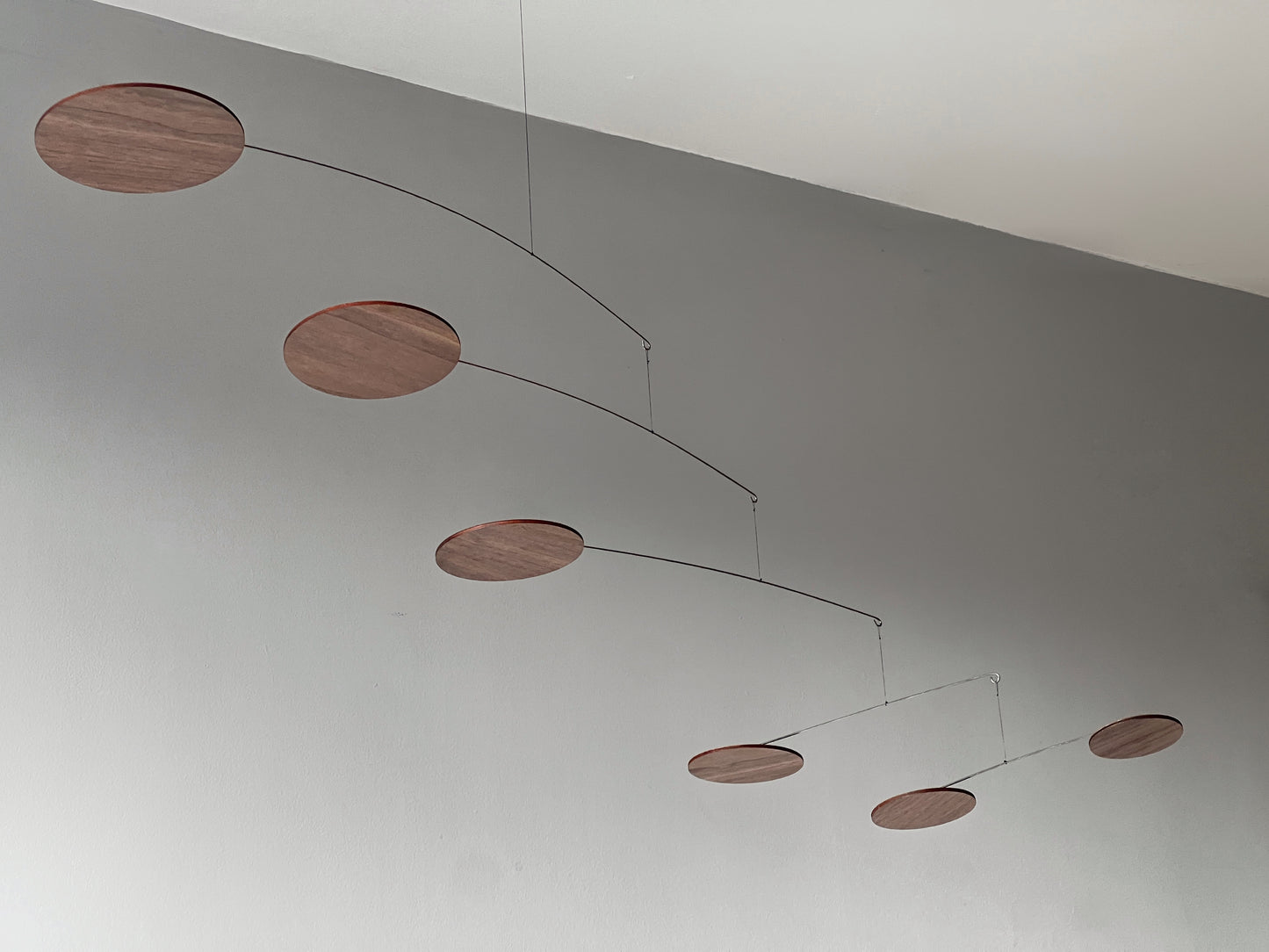 handcrafted walnut mobile by The Illuminist. This elegant modern mobile is made from walnut veneer wooden discs, stainless steel wire, carefully balanced to create gentle, floating motion. it’s the perfect piece of designer home decor for modern interiors. Inspired by Alexander Calder’s mobiles, The Orbit blends art and engineering to form a serene kinetic sculpture that transforms as it moves with the air. make it ideal for mid century decor, Scandinavian design, or any minimalist decor