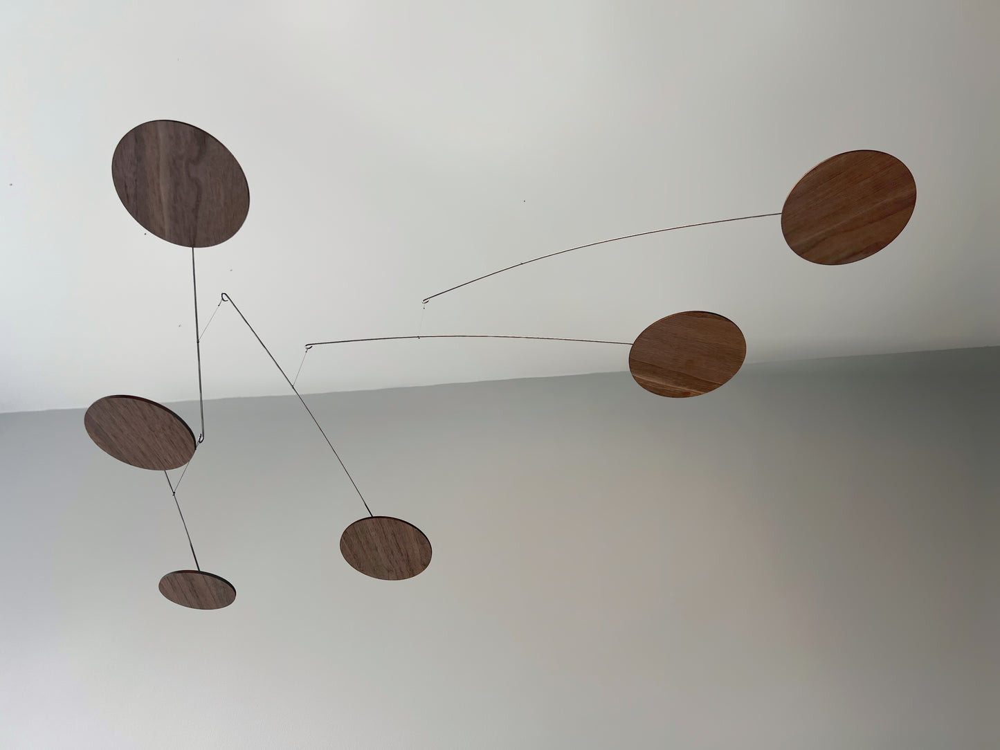 handcrafted walnut mobile by The Illuminist. This elegant modern mobile is made from walnut veneer wooden discs, stainless steel wire, carefully balanced to create gentle, floating motion. it’s the perfect piece of designer home decor for modern interiors. Inspired by Alexander Calder’s mobiles, The Orbit blends art and engineering to form a serene kinetic sculpture that transforms as it moves with the air. make it ideal for mid century decor, Scandinavian design, or any minimalist decor