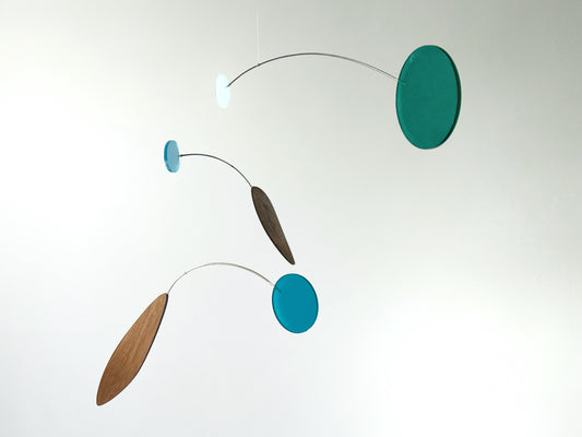 A minimalist mobile with three floating discs and elongated wooden leaves suspended on thin curved metal wires against a plain white background.