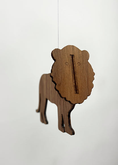 Handmade lion mobile cut from engineered walnut wood with a distinctive mane silhouette, suspended from fine thread as part of a wooden African animal mobile. This lion mobile is one element of a balanced baby mobile designed for nursery decor above a crib or cot. Together with the elephant mobile and giraffe mobile it forms a safari inspired Africa mobile that moves gently in the air like a traditional Flensted mobile. The natural walnut finish makes this wooden mobile a warm, modern hanging.