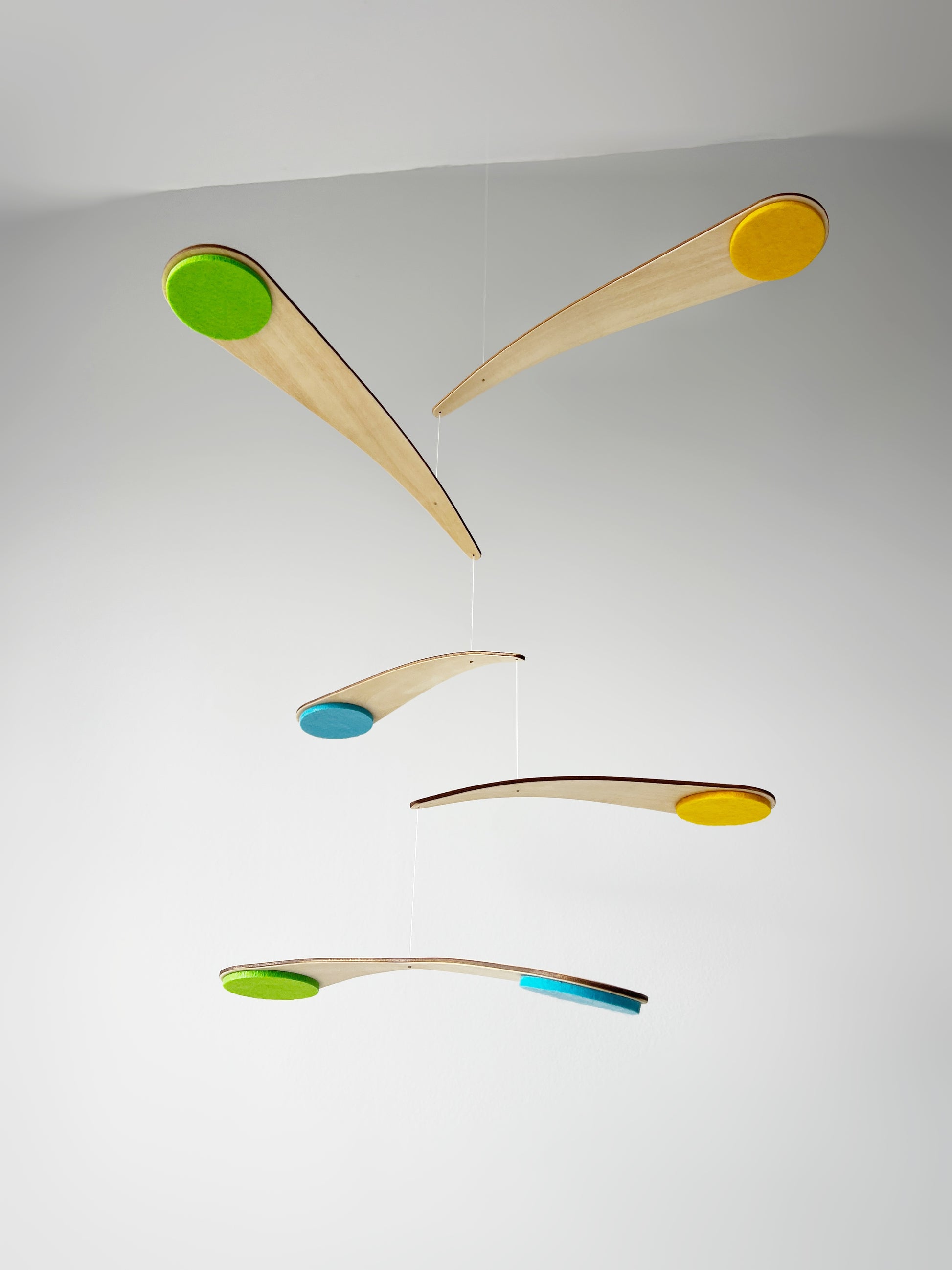 Modern handmade baby mobile hanging above a crib, featuring the Bo Mobile with lightweight curved wooden arms and soft felt circles in custom colours. This spinning nursery mobile is designed from a baby’s point of view, creating a calming floating effect as it gently moves. Ideal for Scandinavian nursery decor, Montessori baby rooms, and minimalist interiors, this wooden crib mobile adds soft movement, visual stimulation, and contemporary style to a modern baby nursery.