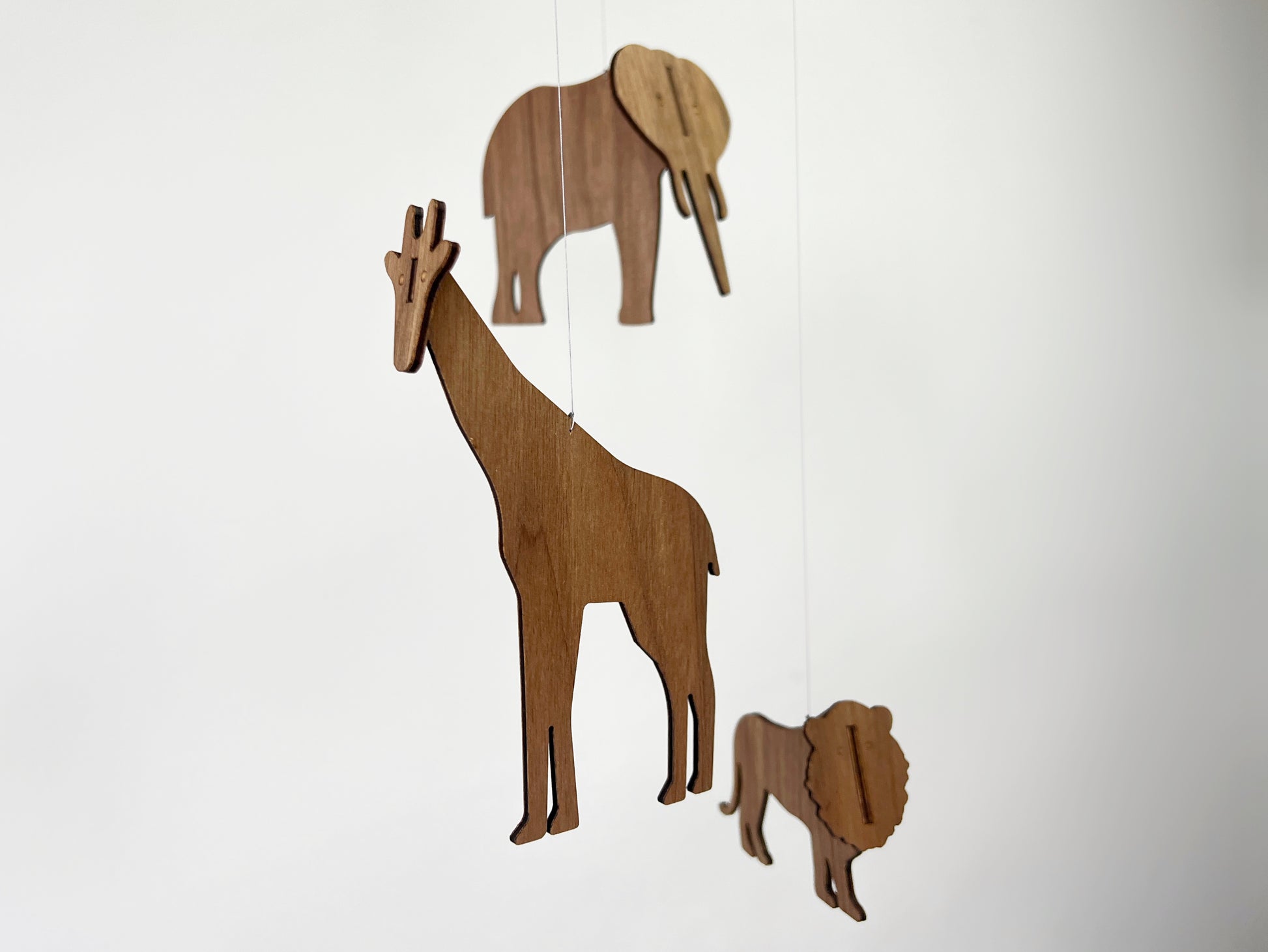 Handmade African animal mobile crafted from engineered walnut wood featuring a giraffe, elephant and lion gently hanging from minimalist rods. This wooden baby mobile is designed as modern nursery decor and a calming hanging mobile for a crib or cot. The natural wood grain gives a warm Scandinavian feel inspired by classic Flensted mobile design. Perfect as an Africa mobile for safari themed nurseries, it combines elephant mobile, giraffe mobile and lion mobile elements in one balanced  mobile