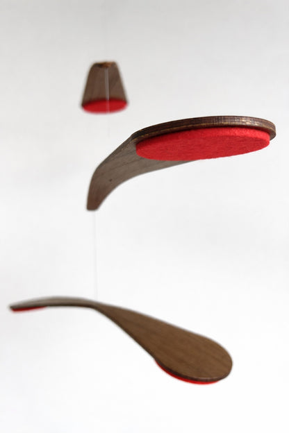 in red felt this Alternative baby mobile in rich walnut wood, featuring curved forms and a floating kinetic structure. This handcrafted nursery decor piece rotates gently, creating a peaceful sensory experience for babies. Inspired by vintage mid century modern design, it works in minimalist and design-led homes. A unique heirloom gift with custom colours available.