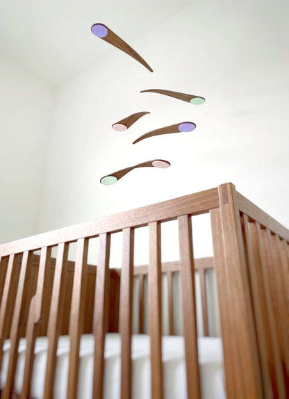 Unique walnut baby mobile combining sculptural design with gentle movement. This kinetic nursery piece rotates in a smooth, balanced motion, creating a calming focal point above a crib or in a living space. Inspired by retro modern art, it suits alternative interiors. Handmade and available in custom colours to match your style.