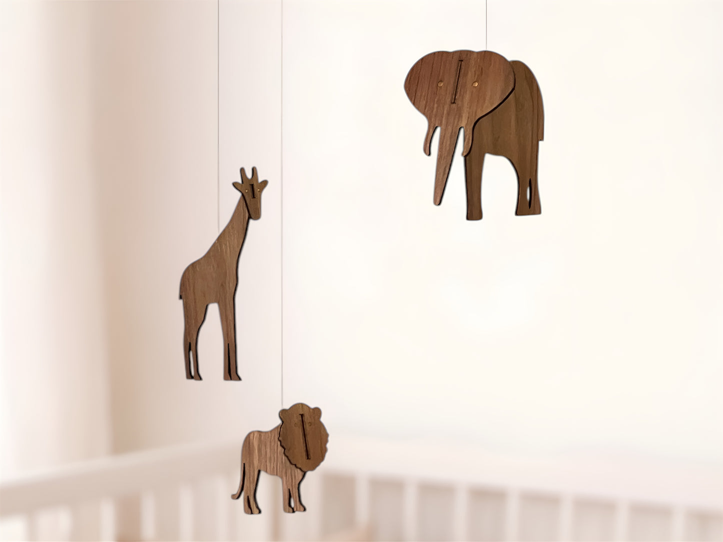Wide view of the African animal mobile hanging above a baby cot as nursery decor. The wooden mobile includes elephant mobile, giraffe mobile and lion mobile silhouettes made from engineered walnut wood. Suspended from minimalist rods, the hanging mobile moves gently like a classic Flensted mobile, making it perfect as a cot mobile or crib mobile. Designed for safari or Africa themed nurseries, this baby mobile adds warmth and natural style while serving as a thoughtful handmade baby gift.