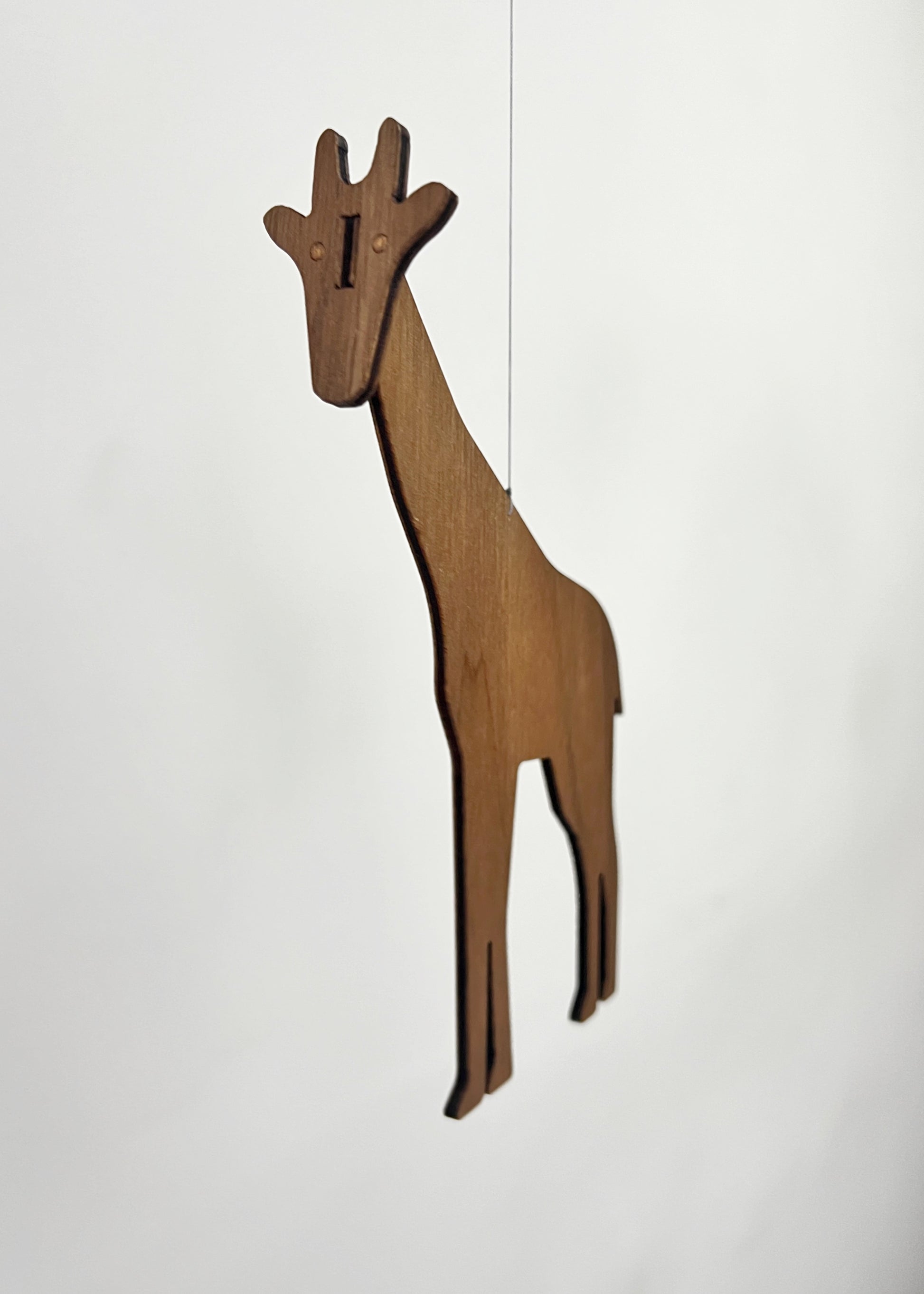 Wooden giraffe mobile piece crafted from engineered walnut, hanging delicately as part of a handmade African animal mobile. The tall giraffe silhouette adds height and elegance to this nursery mobile, designed for modern nursery decor above a baby cot or crib. This wooden baby mobile balances the giraffe with an elephant mobile and lion mobile to create gentle movement like a classic Flensted mobile. Perfect for safari or Africa themed nurseries, this hanging mobile makes a thoughtful baby gift.