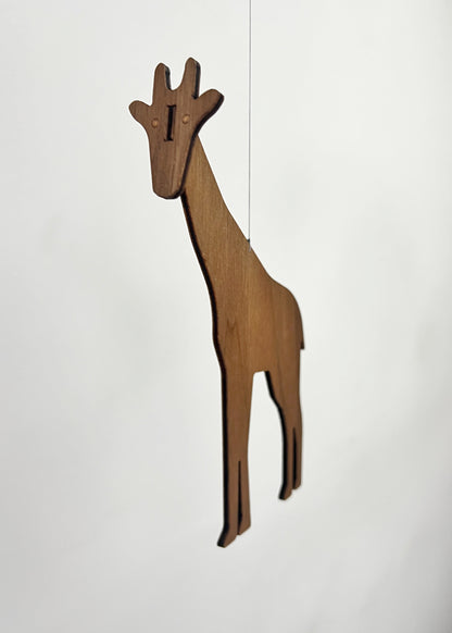 Wooden giraffe mobile piece crafted from engineered walnut, hanging delicately as part of a handmade African animal mobile. The tall giraffe silhouette adds height and elegance to this nursery mobile, designed for modern nursery decor above a baby cot or crib. This wooden baby mobile balances the giraffe with an elephant mobile and lion mobile to create gentle movement like a classic Flensted mobile. Perfect for safari or Africa themed nurseries, this hanging mobile makes a thoughtful baby gift.