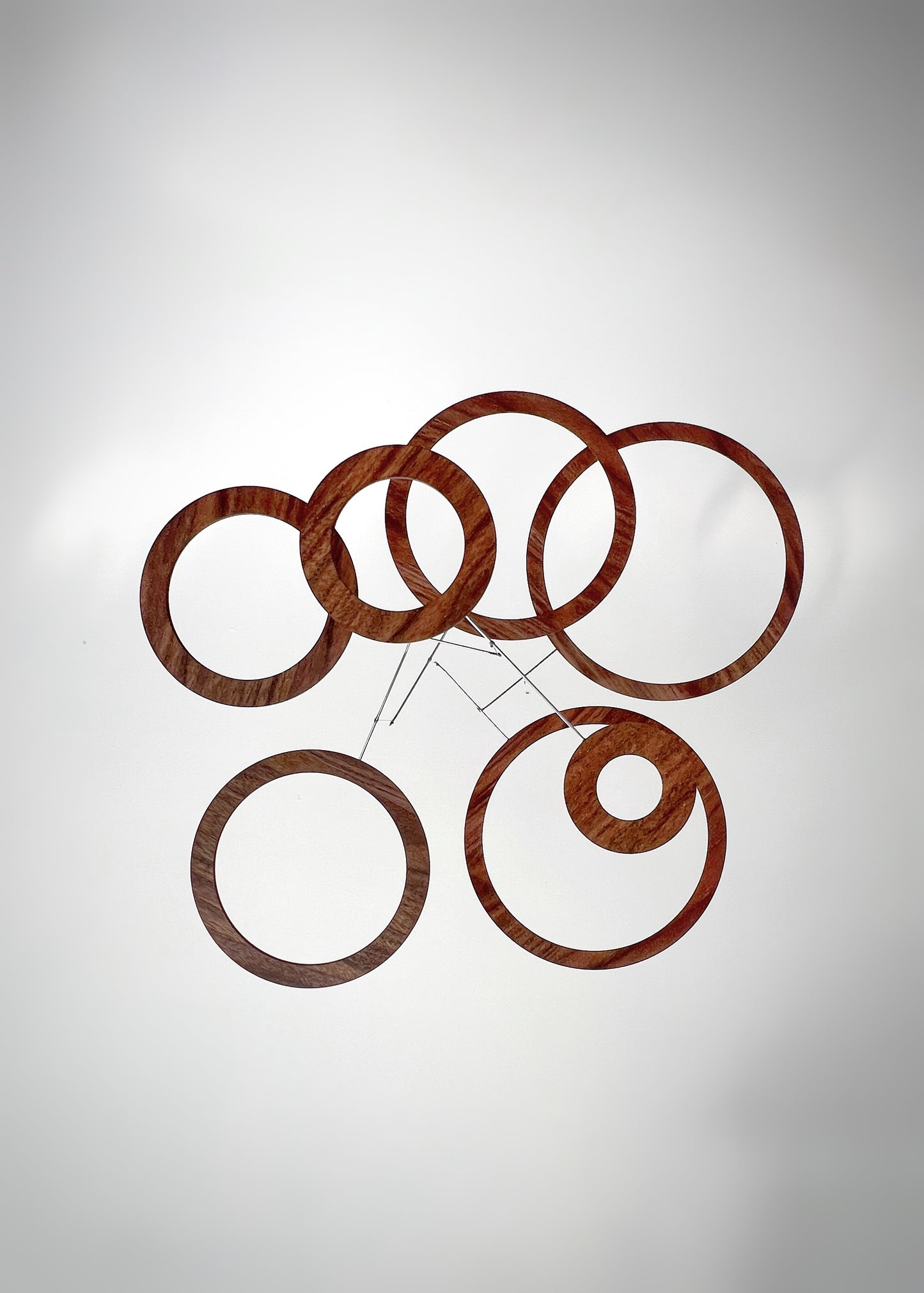 Walnut wood kinetic mobile captured mid-rotation, showing the gentle movement created by natural air currents. Hand-balanced stainless steel rods allow the rings to drift and return to equilibrium. The meditative motion makes this a calming focal point in yoga studios, Pilates spaces, mindfulness rooms, and modern architectural home office or living spaces.