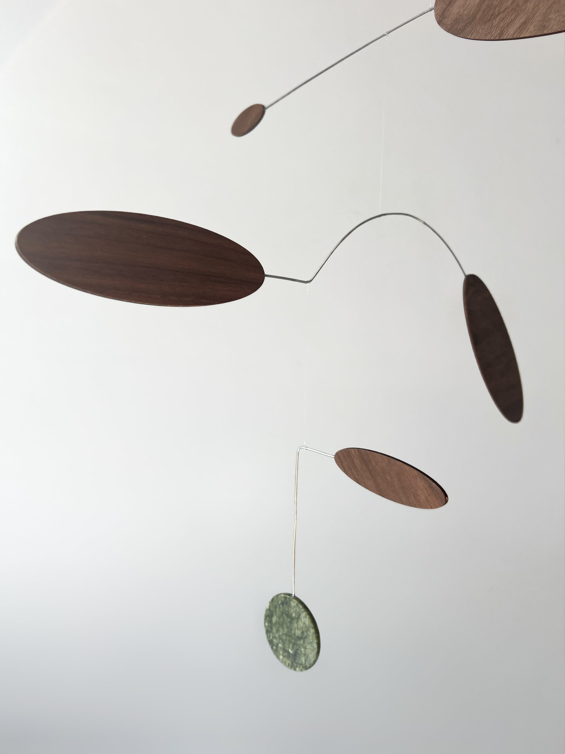 A minimalist mobile with organic-shaped wooden and stone discs suspended on thin metal wires against a plain white background.