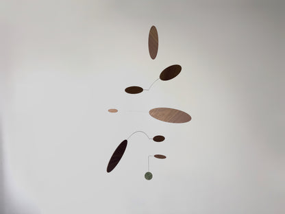 A minimalist mobile with floating oval and circular wooden weights on thin curved wires, suspended against a plain light gray wall.