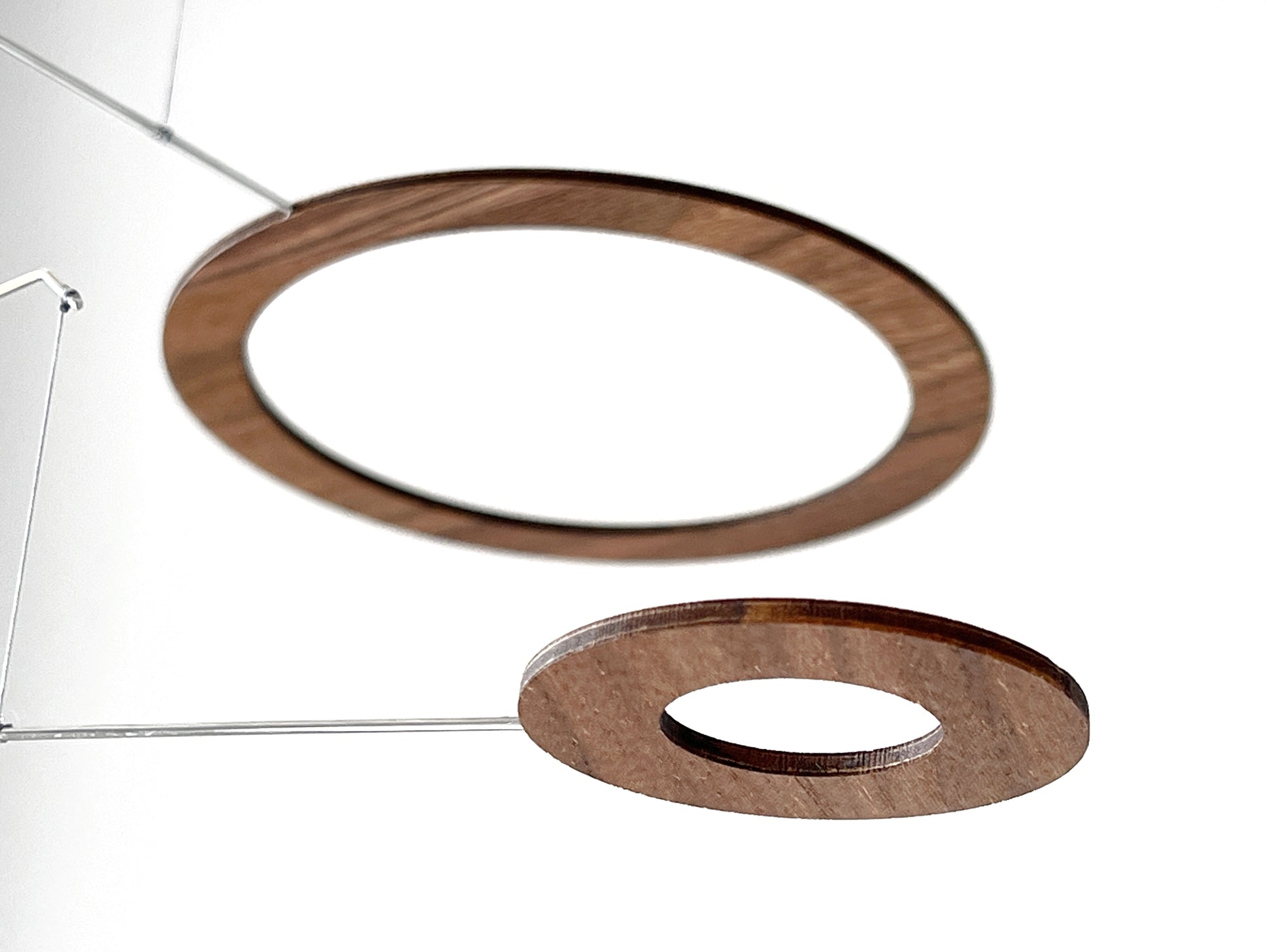 Handmade walnut wood circle mobile hanging above a minimalist home office desk. Five layered walnut veneer rings on stainless steel rods catch natural light from a nearby window. A calm, sculptural ceiling feature for modern home offices, Scandinavian interiors, and design-led spaces. Approx 67cm wide × 30cm tall (26.5 × 11.8 in).