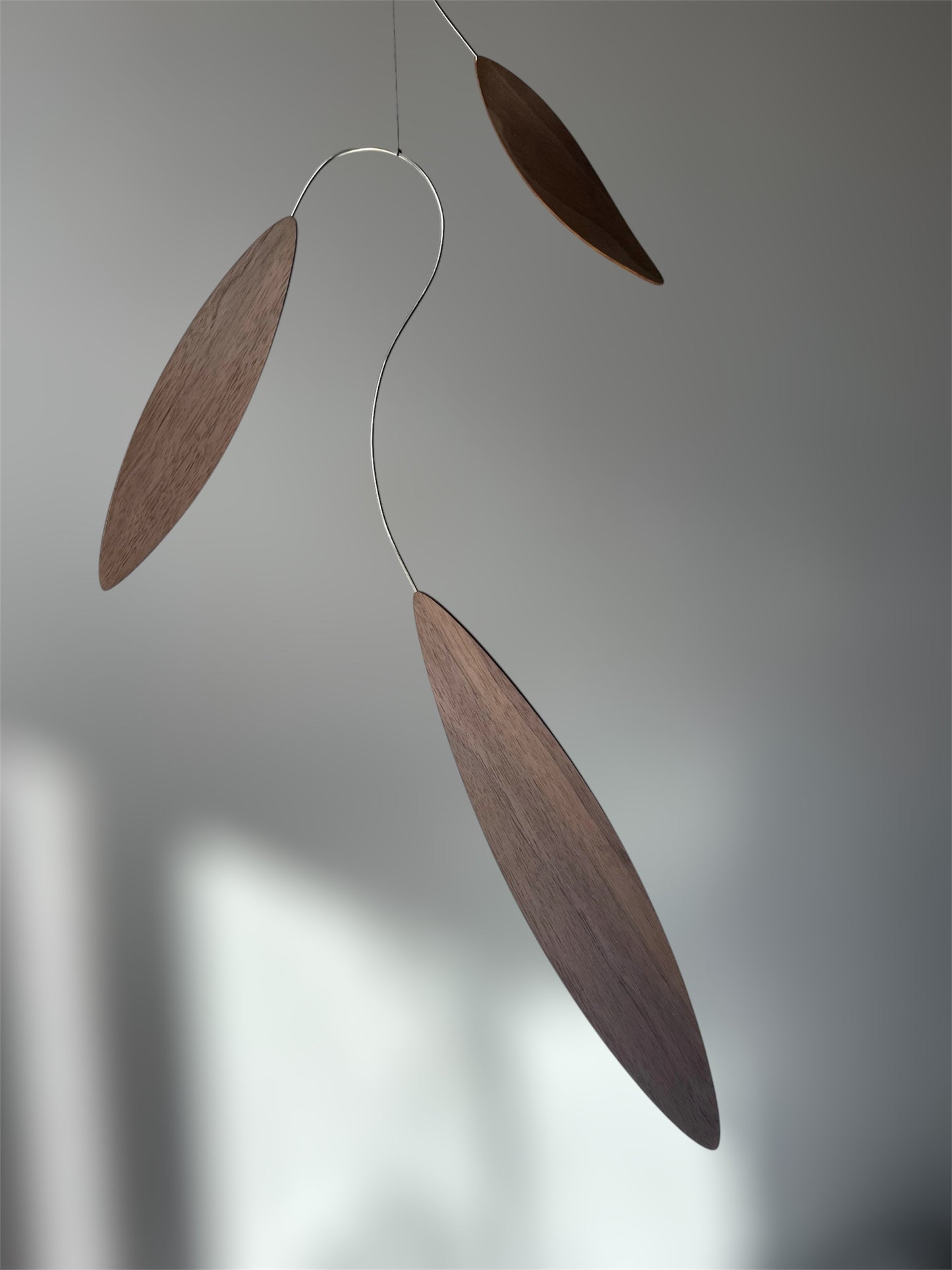 Large 1 metre walnut leaf mobile hanging on a wall beside artist, handcrafted layered walnut veneer wooden mobile with curved leaf forms and stainless steel wire, modern kinetic sculpture, moving art for adults, mid century decor, Scandinavian design minimalist decor, Calder inspired art mobile, unique designer home decor, wood hanging art for living room, gallery wall decor, contemporary mobile handmade in the UK by The Illuminist, soothing balancing art and modern wood art