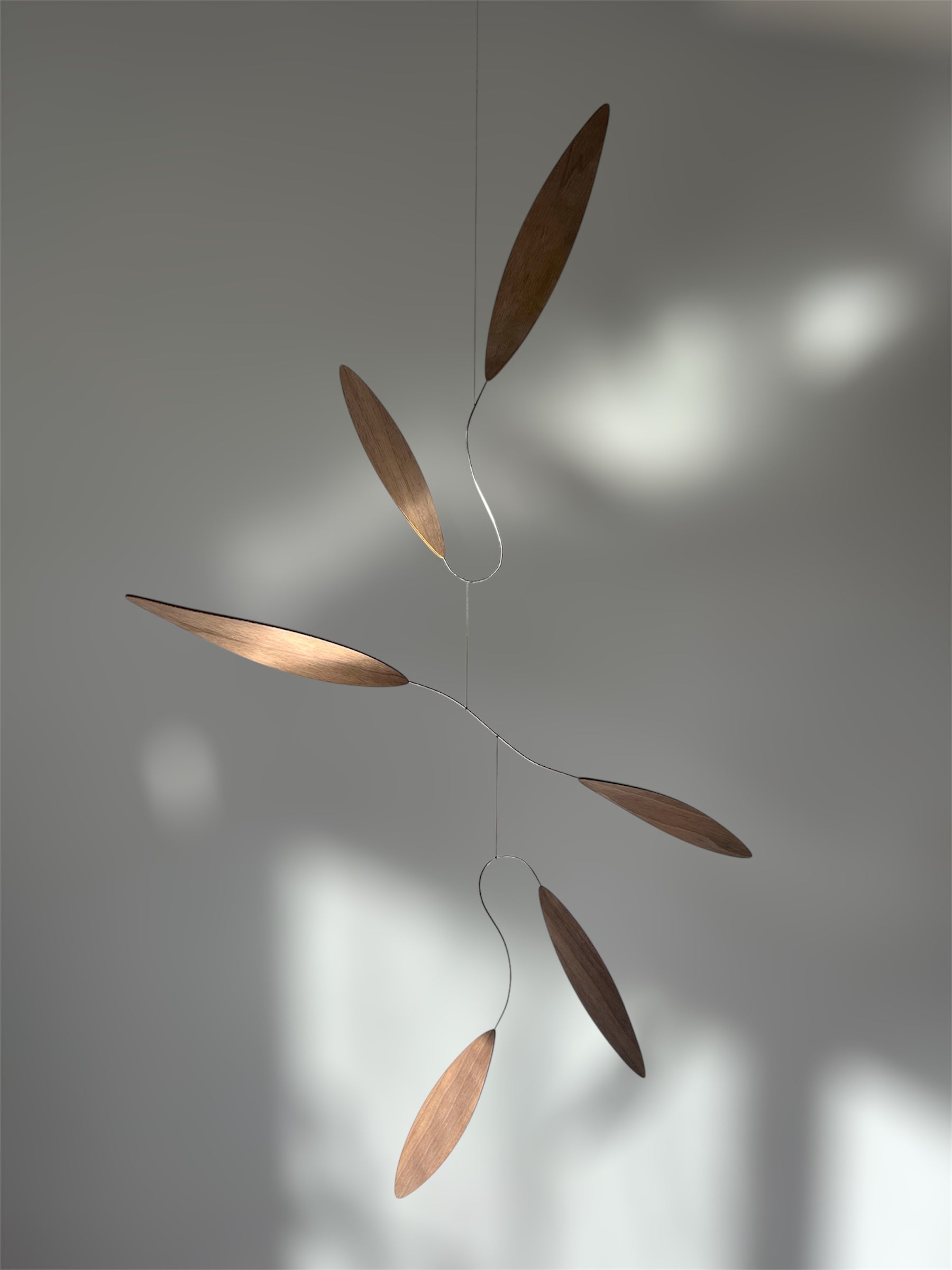 Large 1 metre walnut leaf mobile hanging on a wall beside artist, handcrafted layered walnut veneer wooden mobile with curved leaf forms and stainless steel wire, modern kinetic sculpture, moving art for adults, mid century decor, Scandinavian design minimalist decor, Calder inspired art mobile, unique designer home decor, wood hanging art for living room, gallery wall decor, contemporary mobile handmade in the UK by The Illuminist, soothing balancing art and modern wood art