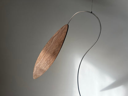 Large 1 metre walnut leaf mobile hanging on a wall beside artist, handcrafted layered walnut veneer wooden mobile with curved leaf forms and stainless steel wire, modern kinetic sculpture, moving art for adults, mid century decor, Scandinavian design minimalist decor, Calder inspired art mobile, unique designer home decor, wood hanging art for living room, gallery wall decor, contemporary mobile handmade in the UK by The Illuminist, soothing balancing art and modern wood art
