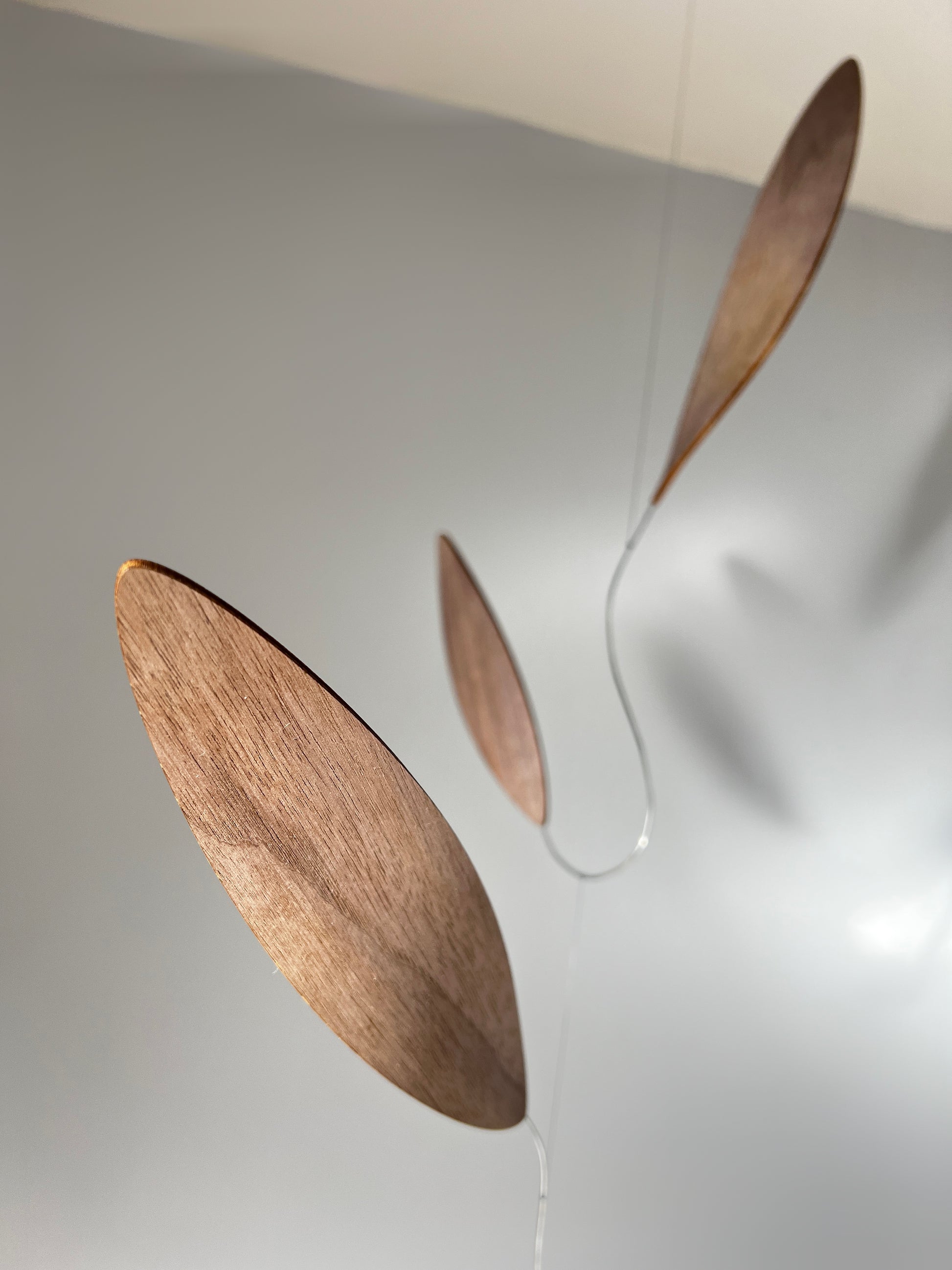 Large 1 metre walnut leaf mobile hanging on a wall beside artist, handcrafted layered walnut veneer wooden mobile with curved leaf forms and stainless steel wire, modern kinetic sculpture, moving art for adults, mid century decor, Scandinavian design minimalist decor, Calder inspired art mobile, unique designer home decor, wood hanging art for living room, gallery wall decor, contemporary mobile handmade in the UK by The Illuminist, soothing balancing art and modern wood art