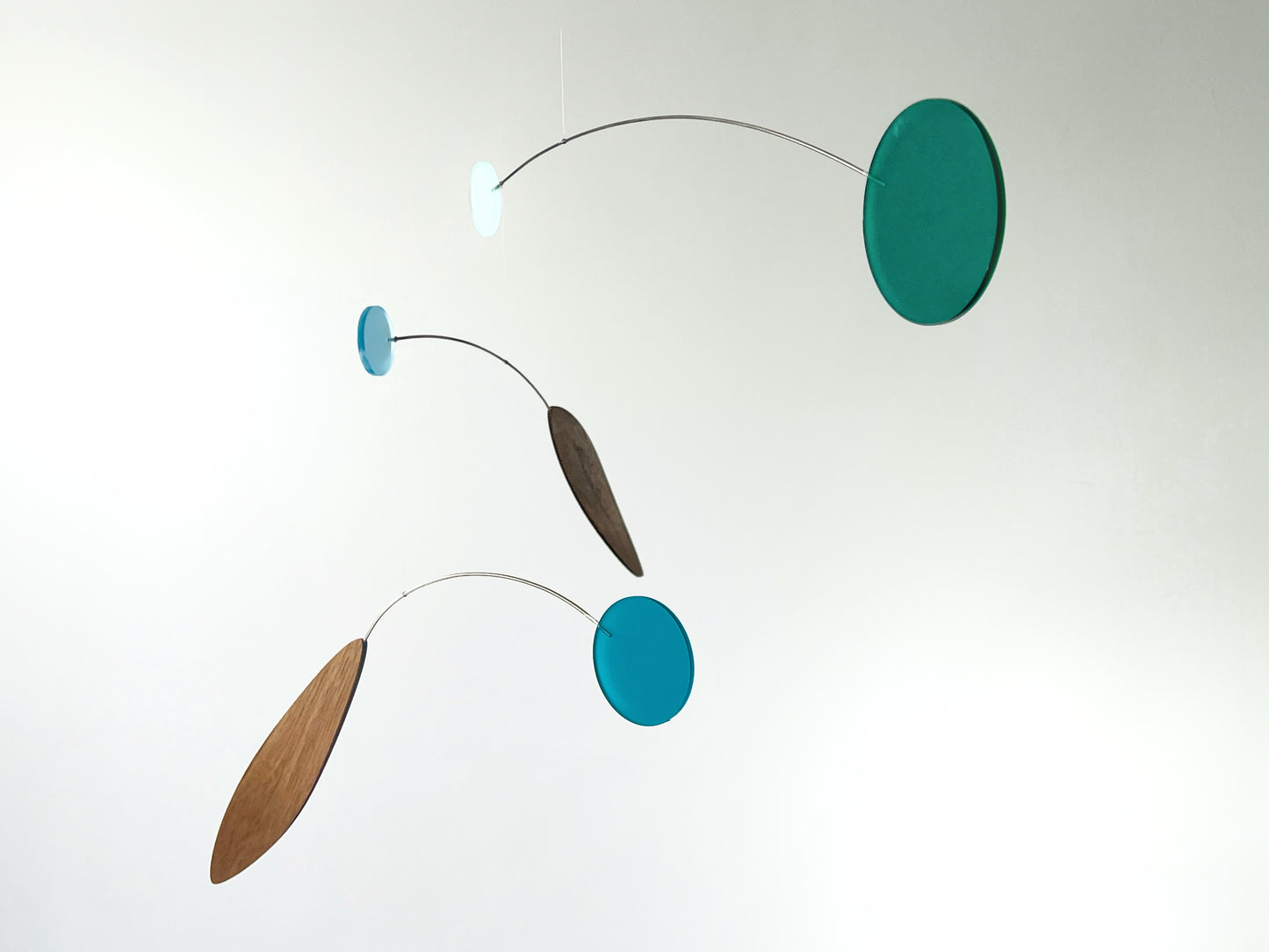 A minimalist mobile with three floating discs and elongated wooden leaves suspended on thin curved metal wires against a plain white background.
