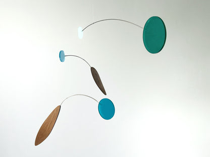 A minimalist mobile with three floating discs and elongated wooden leaves suspended on thin curved metal wires against a plain white background.
