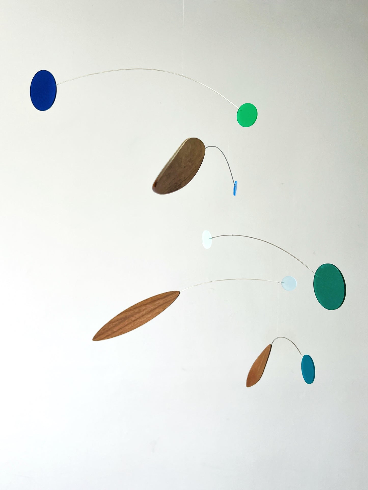 A minimalist abstract mobile with floating wooden and colored discs suspended on fine wires against a plain white wall.