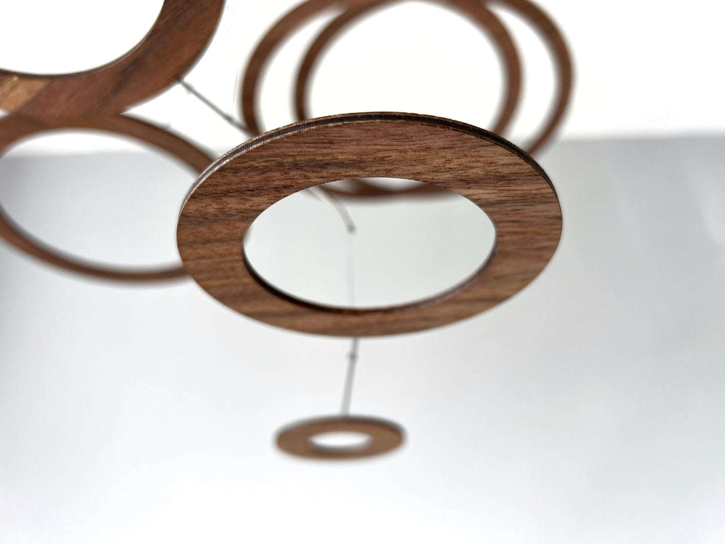 Close-up of a walnut veneer ring from a handmade ceiling mobile, showing warm chocolate-brown wood grain with natural variation. Each ring is hand-cut and lightly sanded — no two pieces share the same grain pattern. A one-of-a-kind sculptural object ideal for interior designers and architects sourcing bespoke handmade décor for residential or commercial projects.